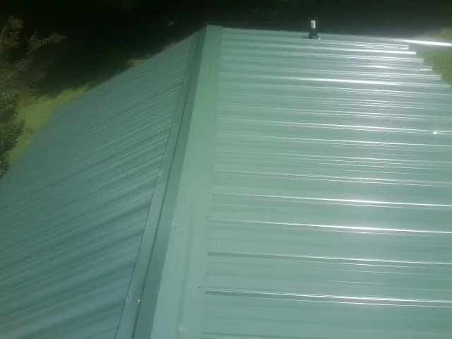 New green metal panels meeting at the ridge of a roof — Flat Roof Repair work by our crew in Smithville