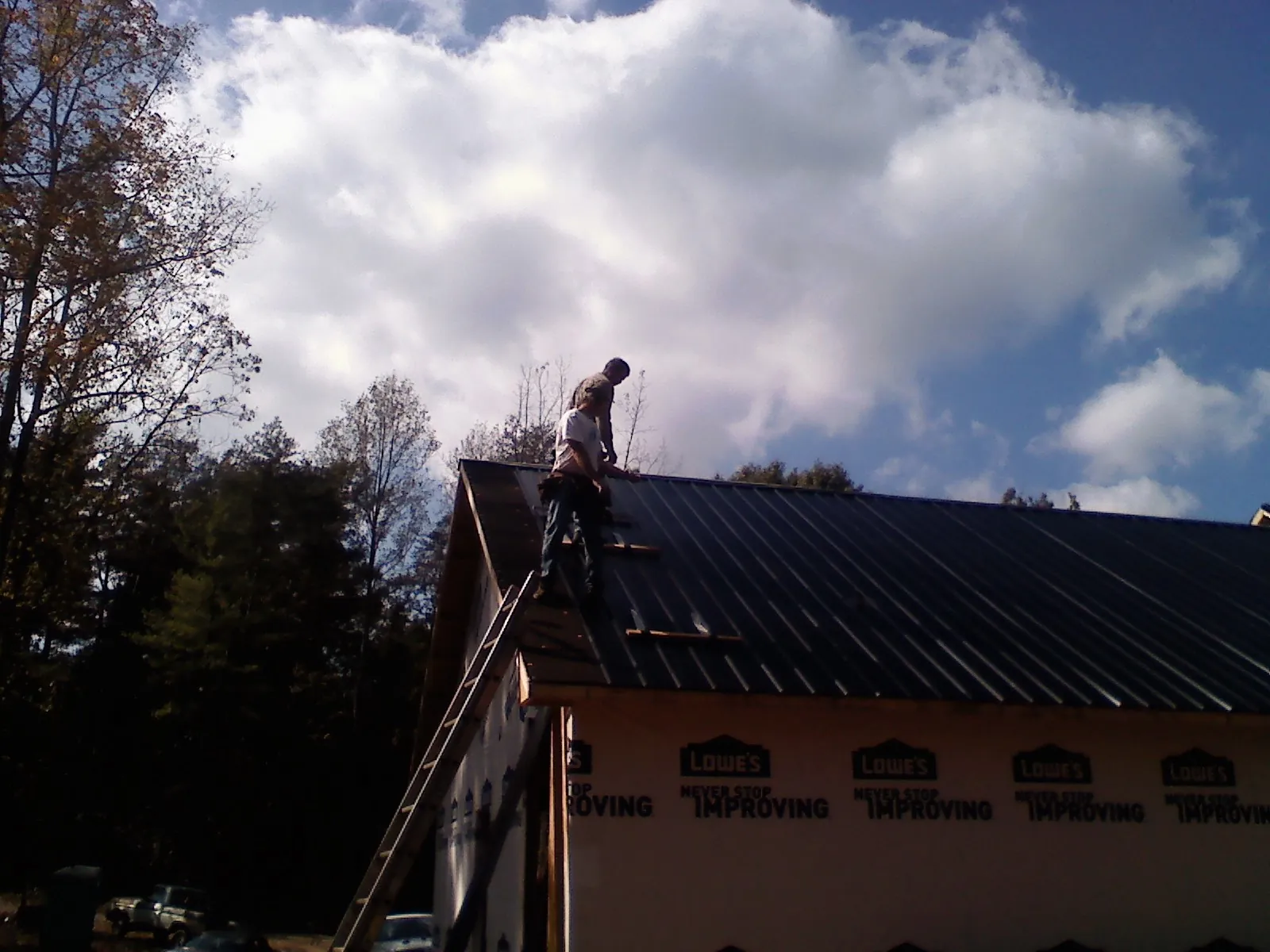 Roofer fastening dark metal panels high against a cloudy sky, from a Roof Inspection job in Smithville